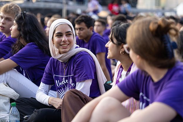 A group of students smiling at each other wearing purple Western University shirts